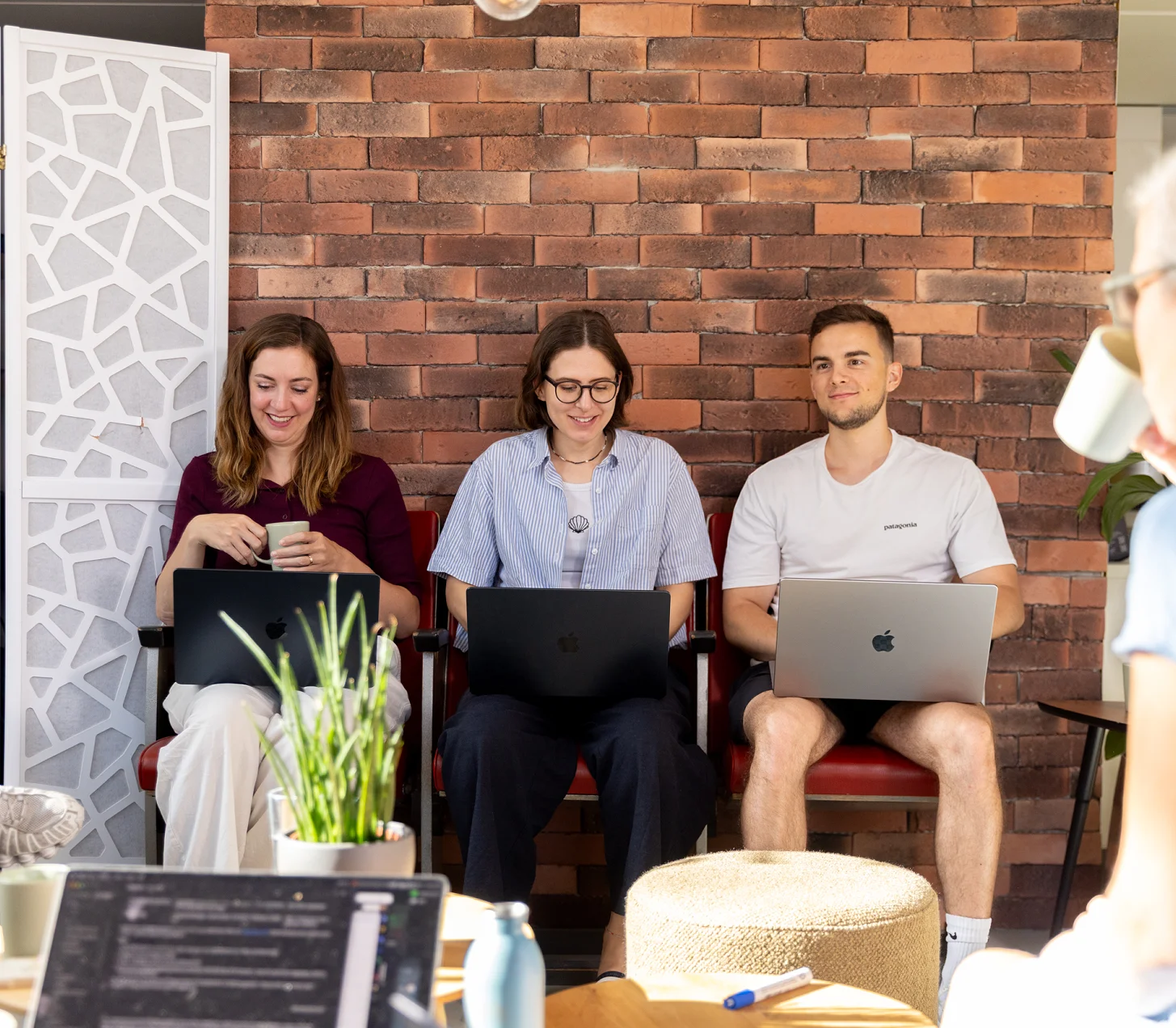 Drei Mitarbeitende mit Laptops vor der Backsteinwand, rechts im Vordergrund Anita