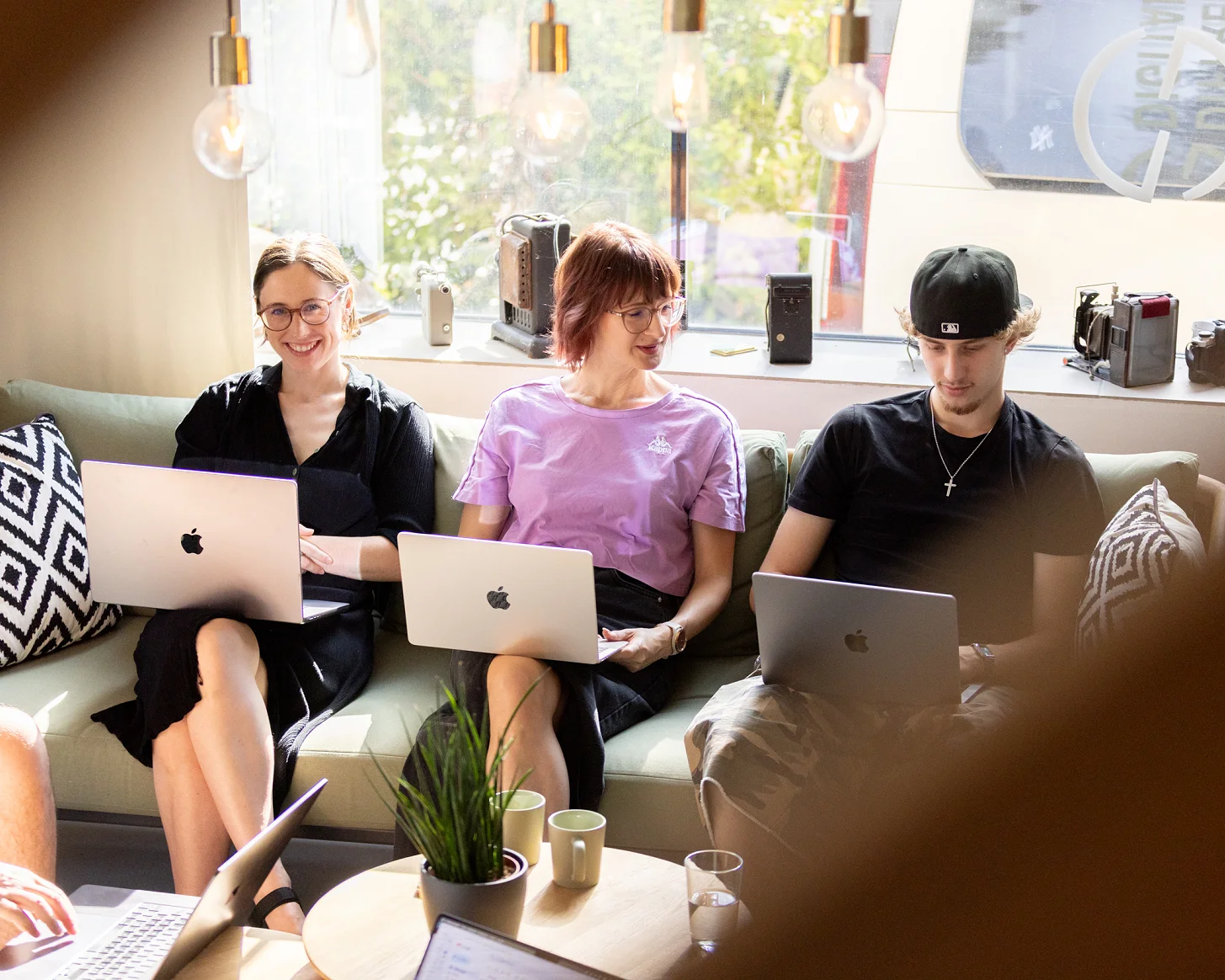 Drei Mitarbeitende arbeiten mit Laptops nebeneinander auf dem Sofa