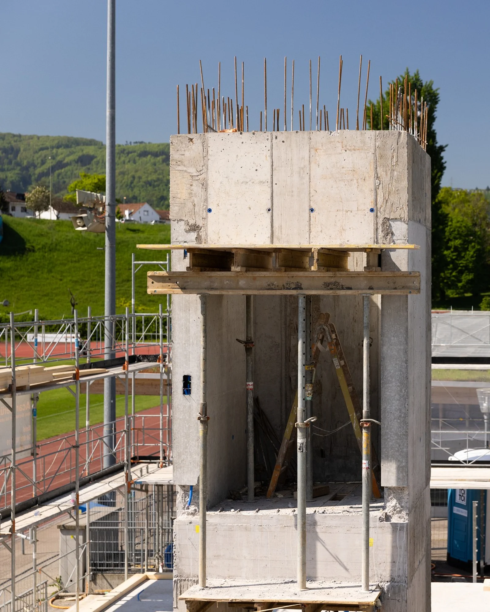 Rohbau des FC-Pratteln-Clubhauses mit Betonkern, Gerüst und Kran, dahinter die Sportanlage
