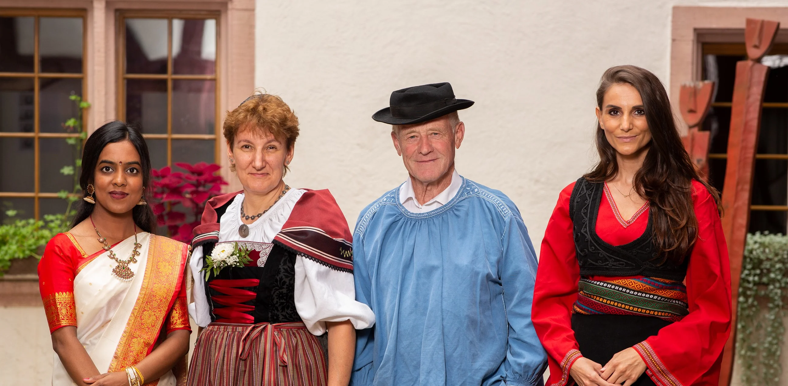 Vier Menschen in Trachten aus verschiedenen Kulturen stehen nebeneinander in einem Innenhof